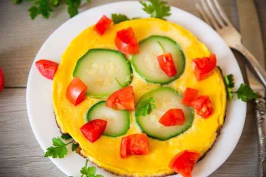 Fried omelet with zucchini, tomatoes, herbs in a plate on a wooden table.