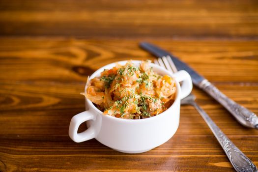 stewed cabbage with carrots and spices in a bowl on a wooden table.