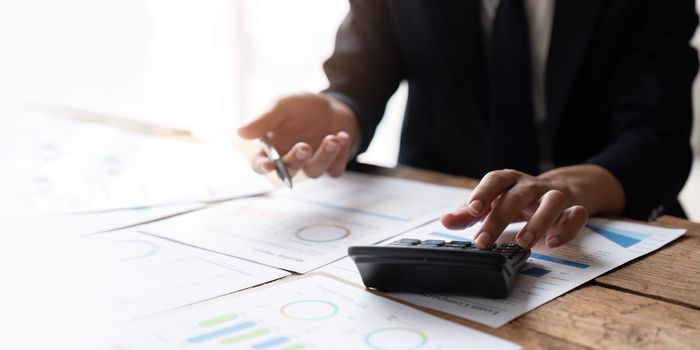 Close up Business man using calculator and laptop for do math finance on wooden desk in office and business working background, tax, accounting, statistics and analytic research concept.