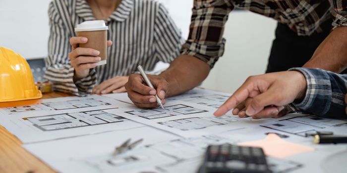 Architect and engineer team working with blueprints for architectural plan, engineer sketching a construction project, green energy concept.