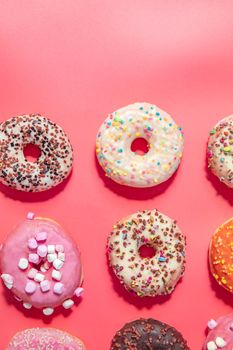 Donuts with icing on pastel pink background. Sweet donuts. top view assorted with various chocolate glazed and sprinkles, sugar sweets concept candy