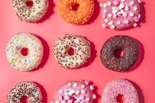 Donuts with icing on pastel pink background. Sweet donuts. top view assorted with various chocolate glazed and sprinkles, sugar sweets concept candy