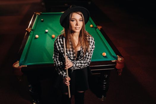 A girl in a hat in a billiard club with a cue in her hands.billiards Game.