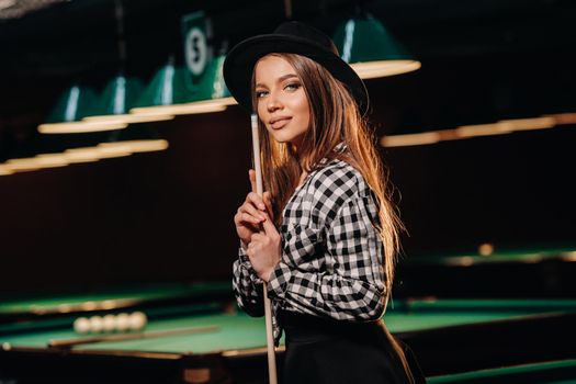 A girl in a hat in a billiard club with a cue in her hands.billiards Game.