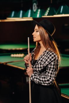 A girl in a hat in a billiard club with a cue in her hands.billiards Game.