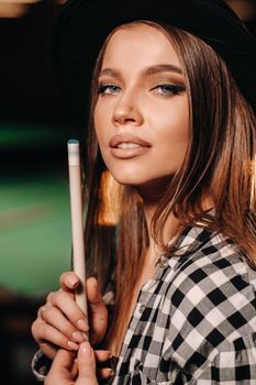 A girl in a hat in a billiard club with a cue in her hands.Pool Game.