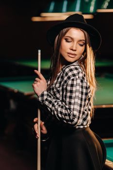 A girl in a hat in a billiard club with a cue in her hands.Pool Game.