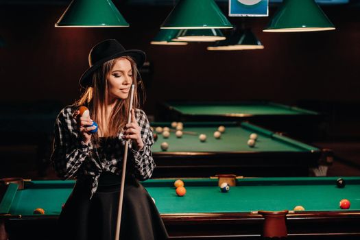 A girl in a hat in a billiard club with a cue in her hands.billiards Game.