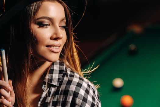 A girl in a hat in a billiard club with a cue in her hands.billiards Game.