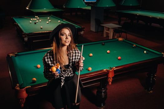 A girl in a hat in a billiard club with a cue in her hands.billiards Game.