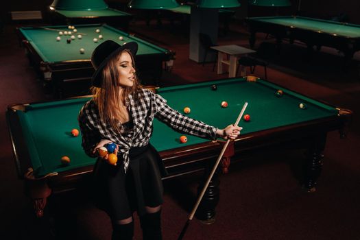 A girl in a hat in a billiard club with a cue in her hands.billiards Game.