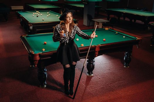 A girl in a hat in a billiard club with a cue in her hands.billiards Game.