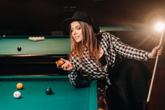 A girl in a hat in a billiard club with a cue and balls in her hands.Playing pool.