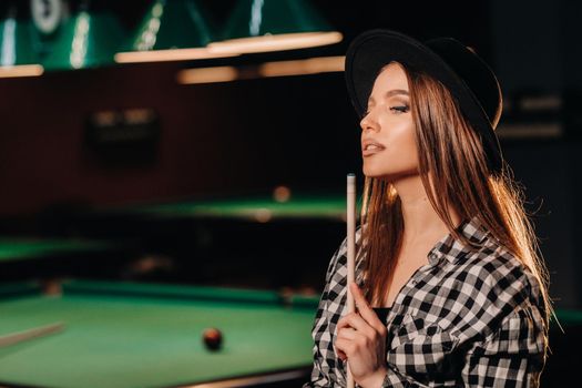 A girl in a hat in a billiard club with a cue in her hands.Pool Game.