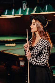 A girl in a hat in a billiard club with a cue in her hands.billiards Game.