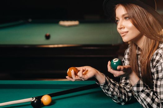 A girl in a hat in a billiard club with balls in her hands.Playing pool.