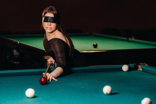 A girl with a blindfold and a cue in her hands in a billiard club.Russian billiards.