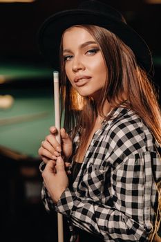 A girl in a hat in a billiard club with a cue in her hands.billiards Game.