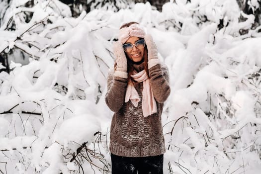 A girl in a sweater and glasses in winter in a snow-covered forest.