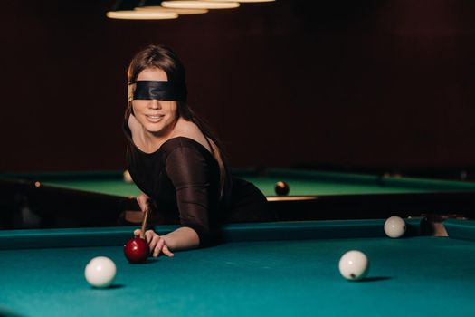 A girl with a blindfold and a cue in her hands in a billiard club.Russian billiards.