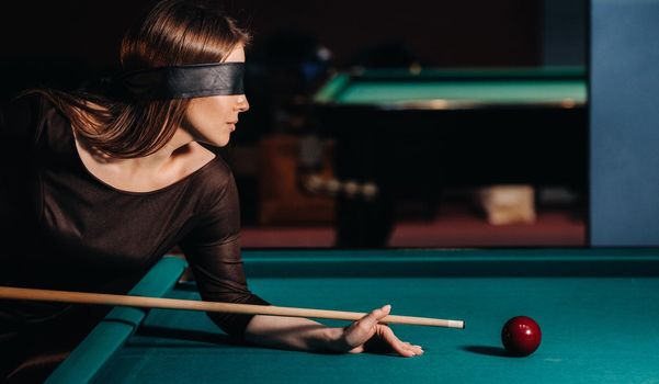 A girl with a blindfold and a cue in her hands in a billiard club.Russian billiards.