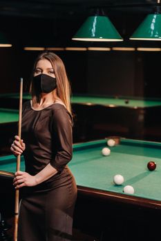 Masked girl in a pool club with a cue in her hands.