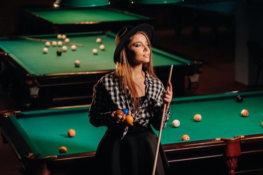 A girl in a hat in a billiard club with a cue in her hands.billiards Game.