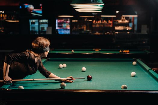 A girl with a blindfold and a cue in her hands in a billiard club.Russian billiards.