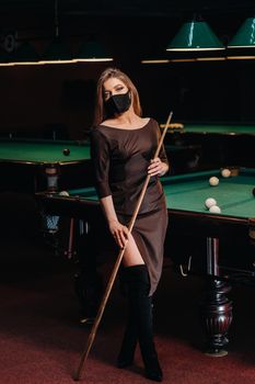 Masked girl in a pool club with a cue in her hands.