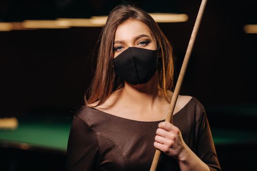 Masked girl in a pool club with a cue in her hands.