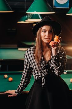A girl in a hat in a billiard club with balls in her hands.Playing pool.