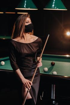 Masked girl in a pool club with a cue in her hands.