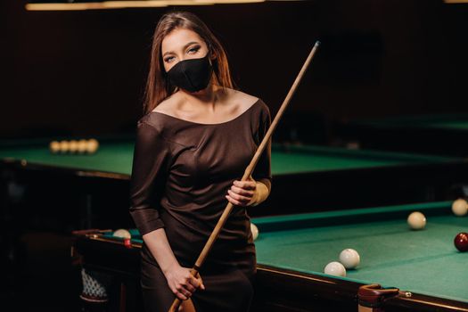 Masked girl in a pool club with a cue in her hands.