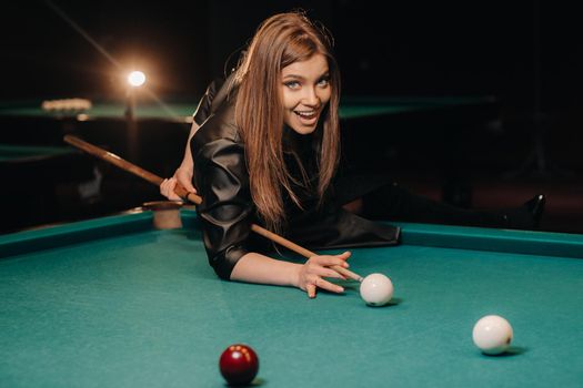 A girl with a cue in her hands makes a shot at a ball in a billiard club.Russian billiards.