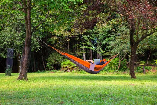 Woman working on her computer lying on hammock