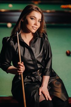 A girl with a cue in her hands sits on a table in a billiard club.Russian billiards.