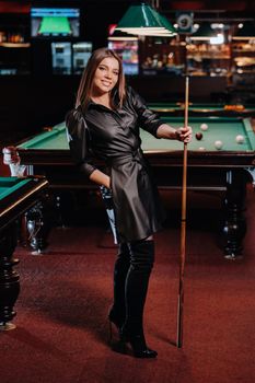 A girl with a cue in her hands is standing in a billiard club.Russian billiards.