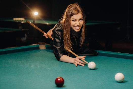 A girl with a cue in her hands makes a shot at a ball in a billiard club.Russian billiards.