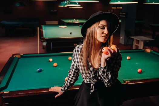 A girl in a hat in a billiard club with balls in her hands.Playing pool.