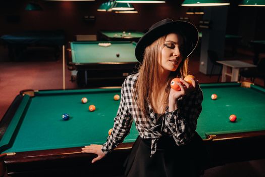 A girl in a hat in a billiard club with balls in her hands.Playing pool.