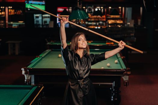 A girl with a cue in her hands is standing in a billiard club.Russian billiards.