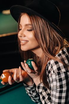 A girl in a hat in a billiard club with balls in her hands.Playing pool.