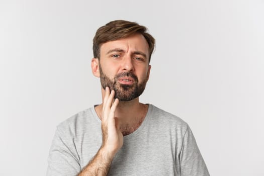 Close-up of confused man touching his beard and looking at himself, need to shave, standing over white background.