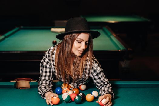 A girl in a hat in a billiard club with balls in her hands.Playing pool.