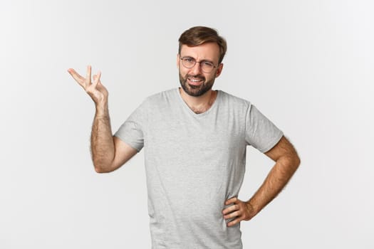 Portrait of handsome adult man looking confused, raising hand up and looking perplexed, standing over white background.