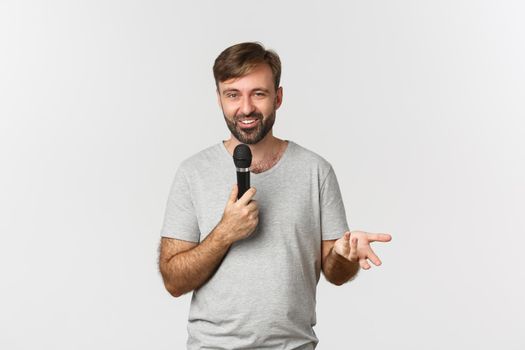 Image of charismatic man in gray t-shirt making a speech, holding microphone and talking, standing over white background.