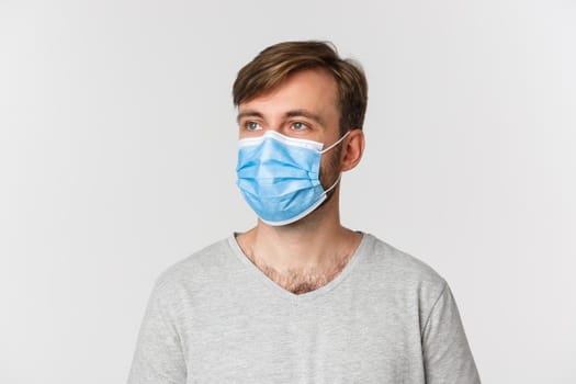 Concept of pandemic, covid-19 and social-distancing. Close-up of handsome man in medical mask, looking left at logo, standing over white background.