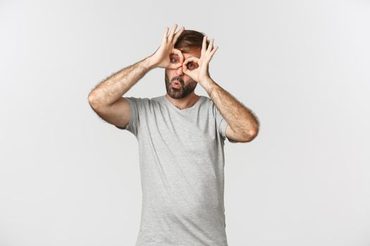 Portrait of funny caucasian guy making faces and mocking someone, standing over white background.