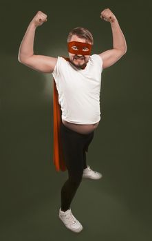 Strong superhero expressing power. Man in white t-shirt, red mask and cape shows biceps while looking at the camera. Isolated on chive green background.