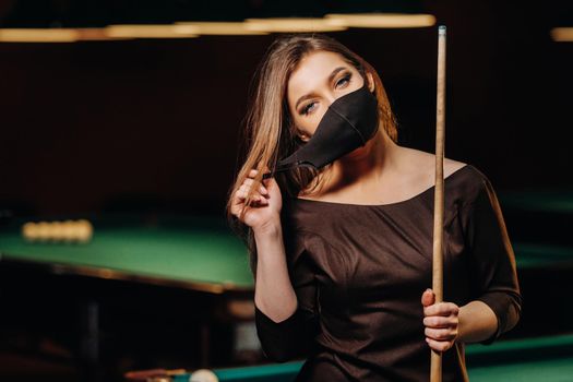 Masked girl in a pool club with a cue in her hands.